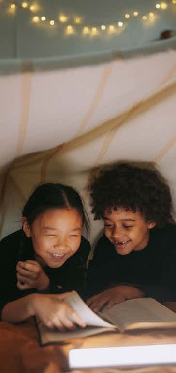 Two children in a tent reading a book